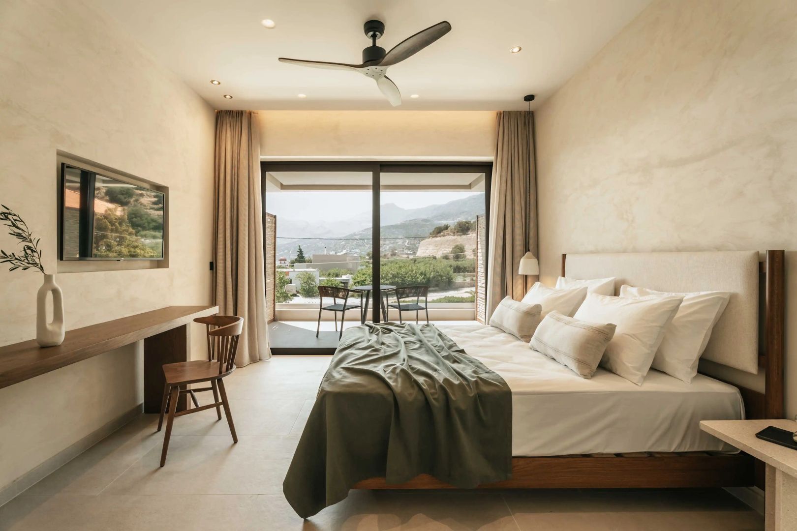 Helles Hotelzimmer mit Doppelbett, Holzschreibtisch und Glas-Schiebetür zur Terrasse.