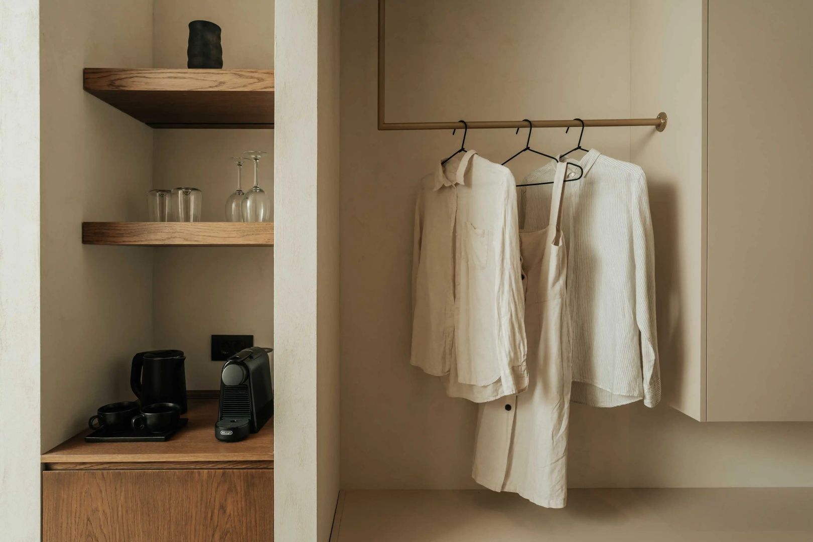 Offener Kleiderschrank mit aufgehängter Kleidung und Holzregal mit Kaffeemaschine.