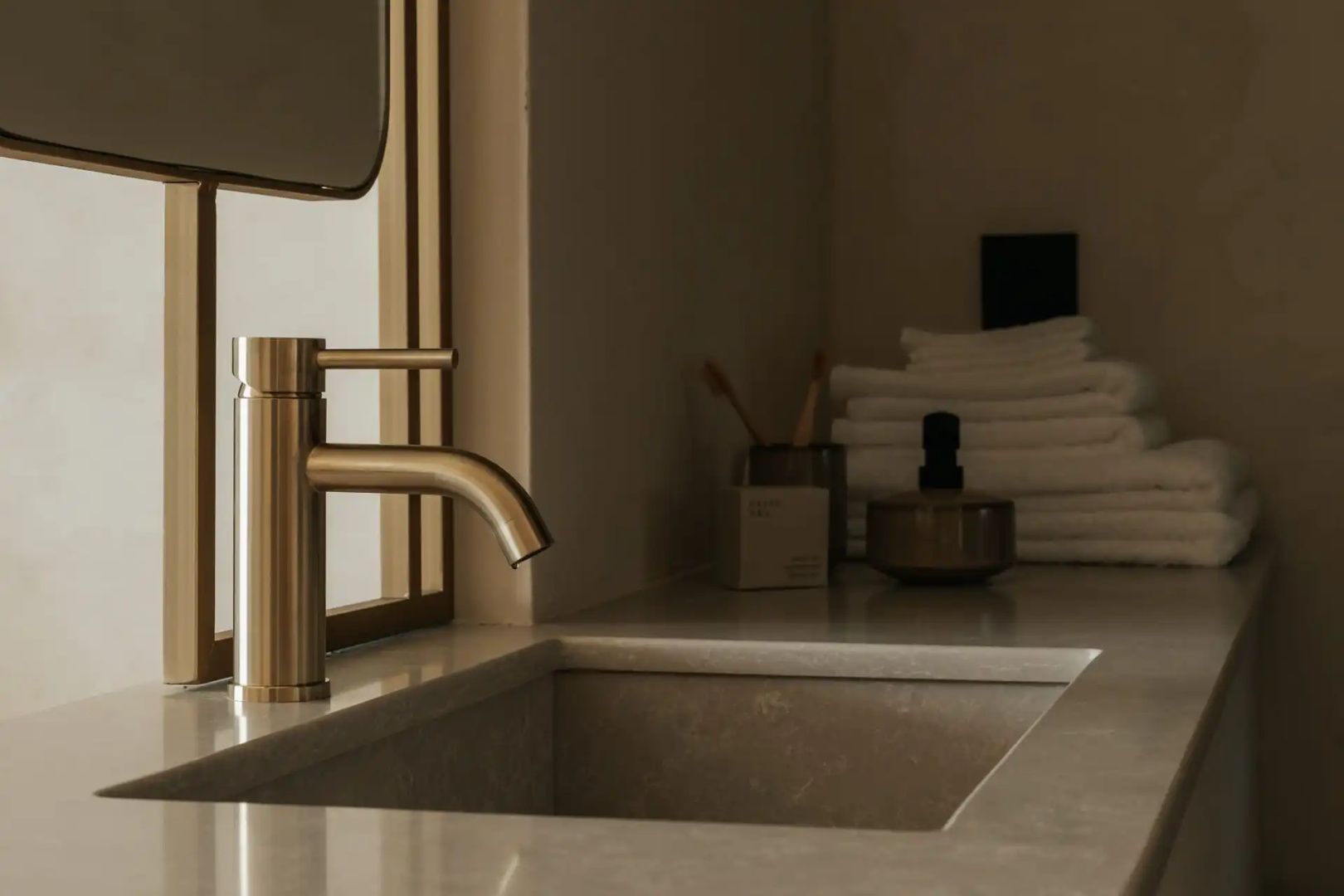 Messing-Wasserhahn an einem Steinwaschbecken im Badezimmer mit gestapelten Handtüchern.