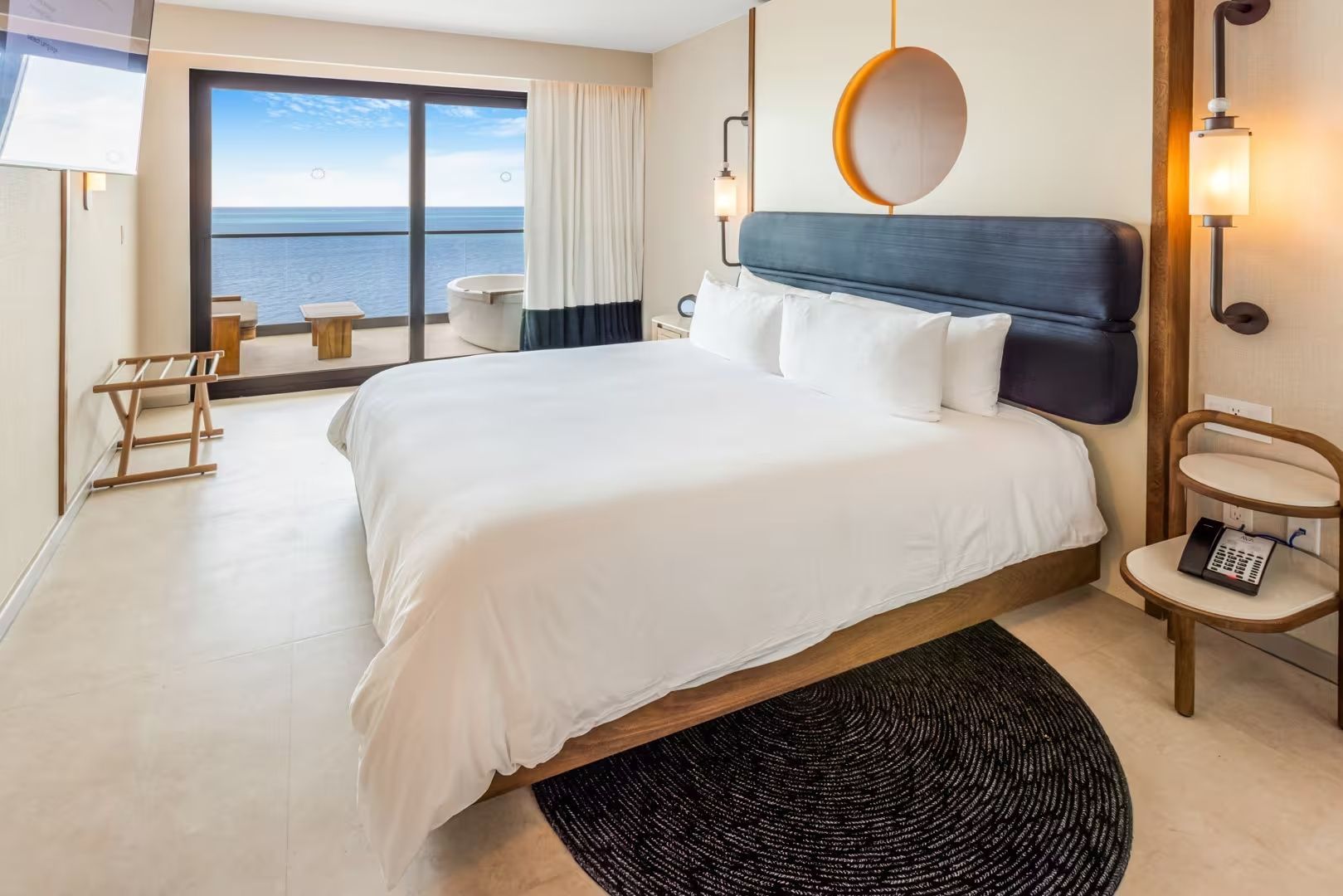 Doppelbett im hellen Hotelzimmer mit Zugang zum Balkon und Blick auf das Meer
