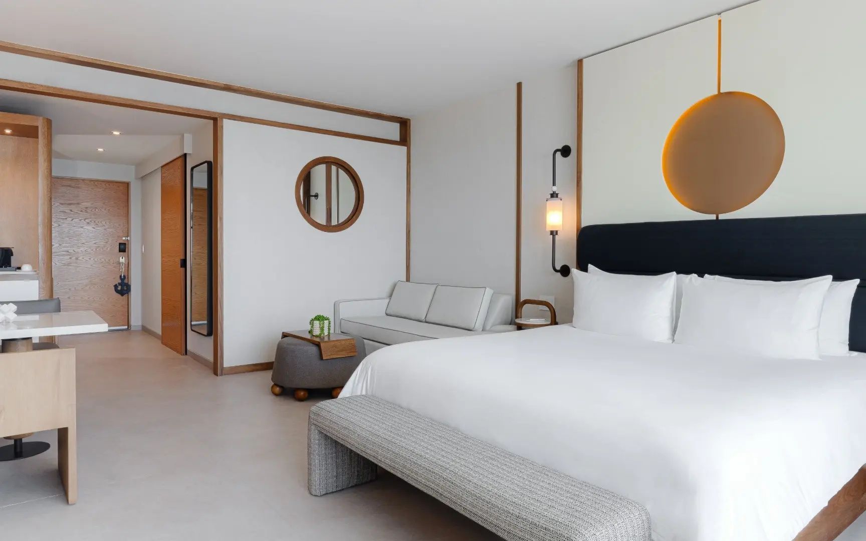 Modernes Hotelzimmer mit großem Doppelbett, hellem Sofa und runder Wanddekoration.