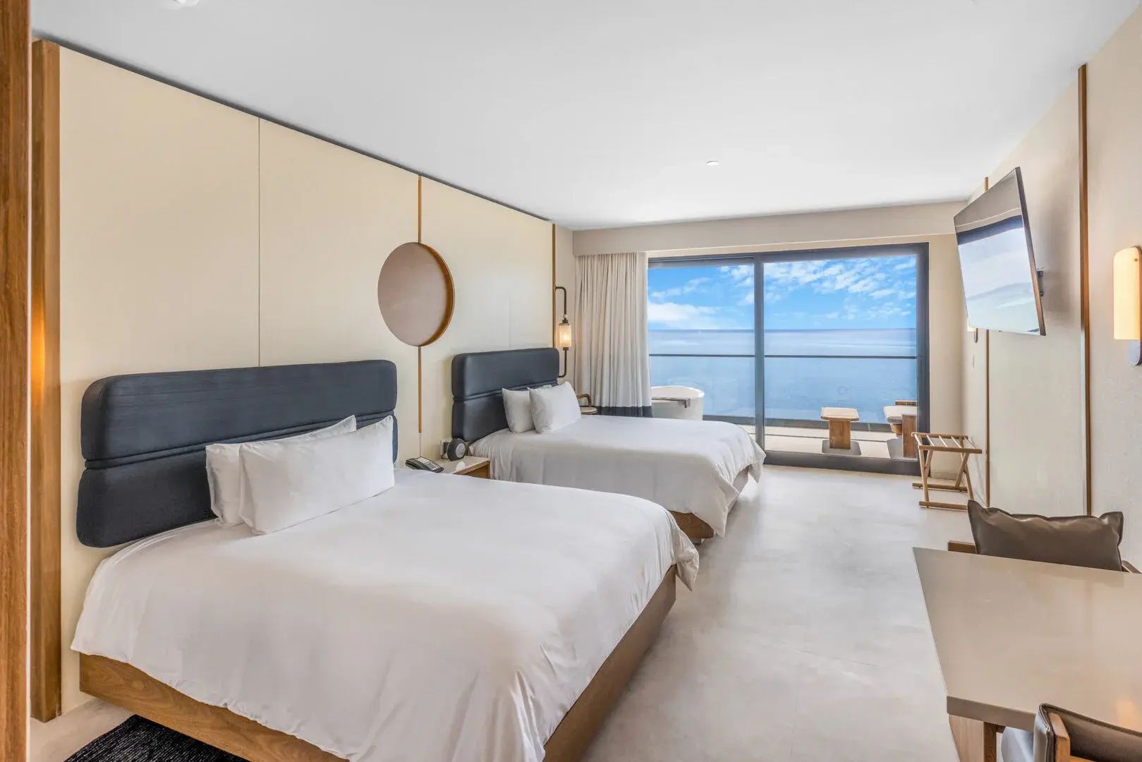 Hotelzimmer mit zwei Doppelbetten und einer großen Fensterscheibe zum Balkon mit Meerblick.