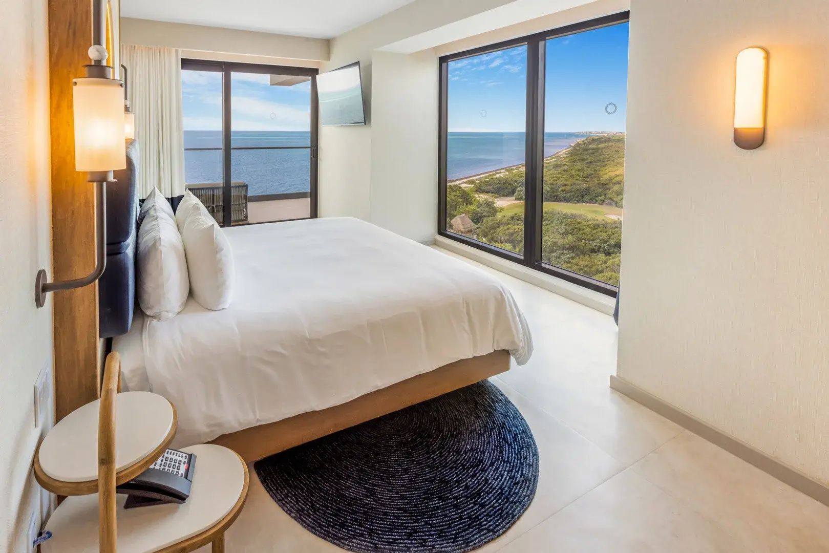Helles Schlafzimmer mit großem Bett und Fenstern mit Blick auf Meer und Natur