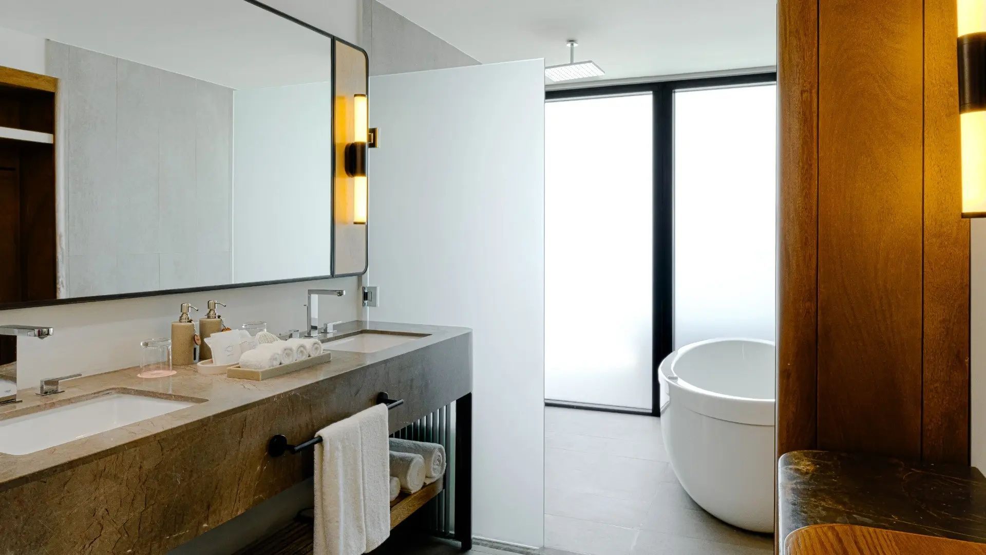 Badezimmer mit moderner freistehender Badewanne, großen Spiegeln und Steinwaschtisch.