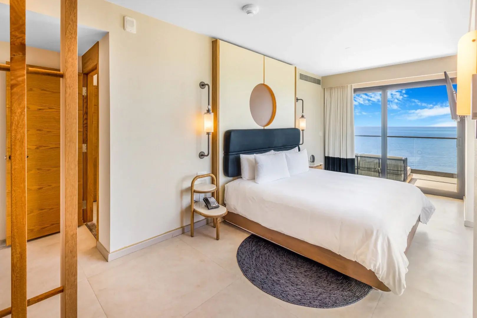 Hotelzimmer mit weiß bezogenem Doppelbett, Nachttischen und Blick Richtung Balkon