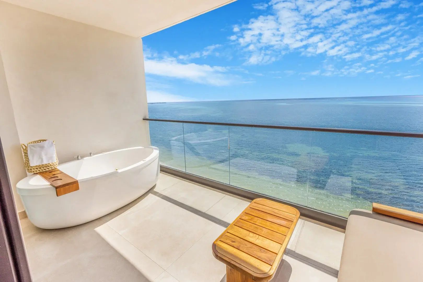 Überdachter Balkon mit frei stehender Badewanne, Holzmöbeln und Blick über den Ozean.