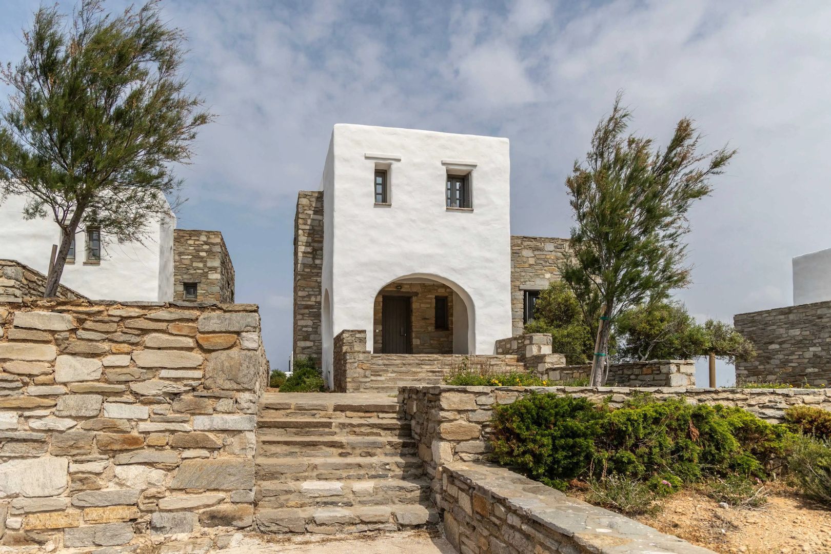 Weiße Villa im kykladischen Stil mit Natursteinmauern und kleiner Treppe zum Eingang.