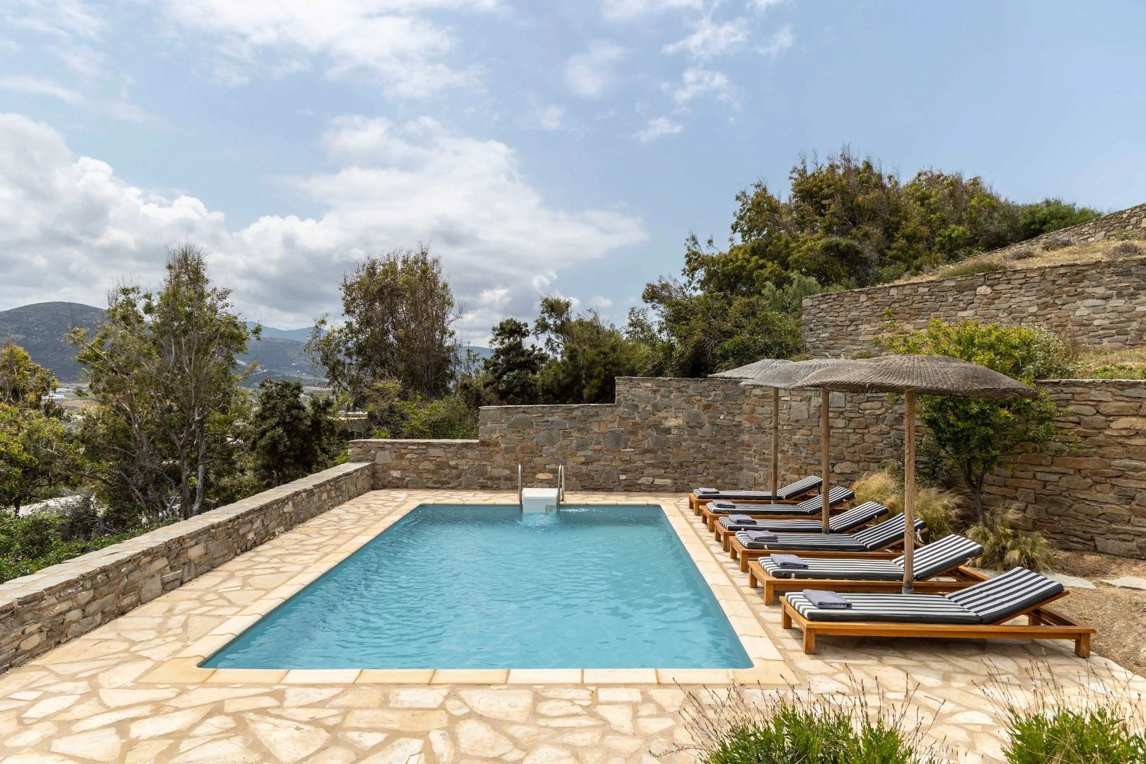 Rechteckiger Pool im Außenbereich umgeben von Sonnenliegen und einer Natursteinmauer.