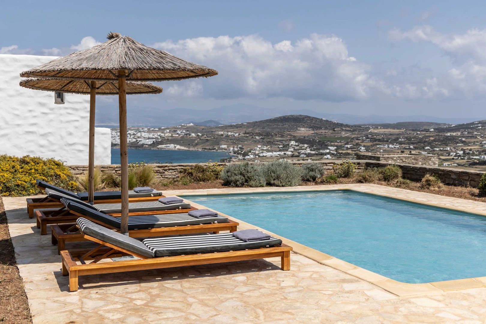 Sonnendeck mit Liegestühlen und Schirmen am Pool mit Blick auf die Küstenlandschaft.