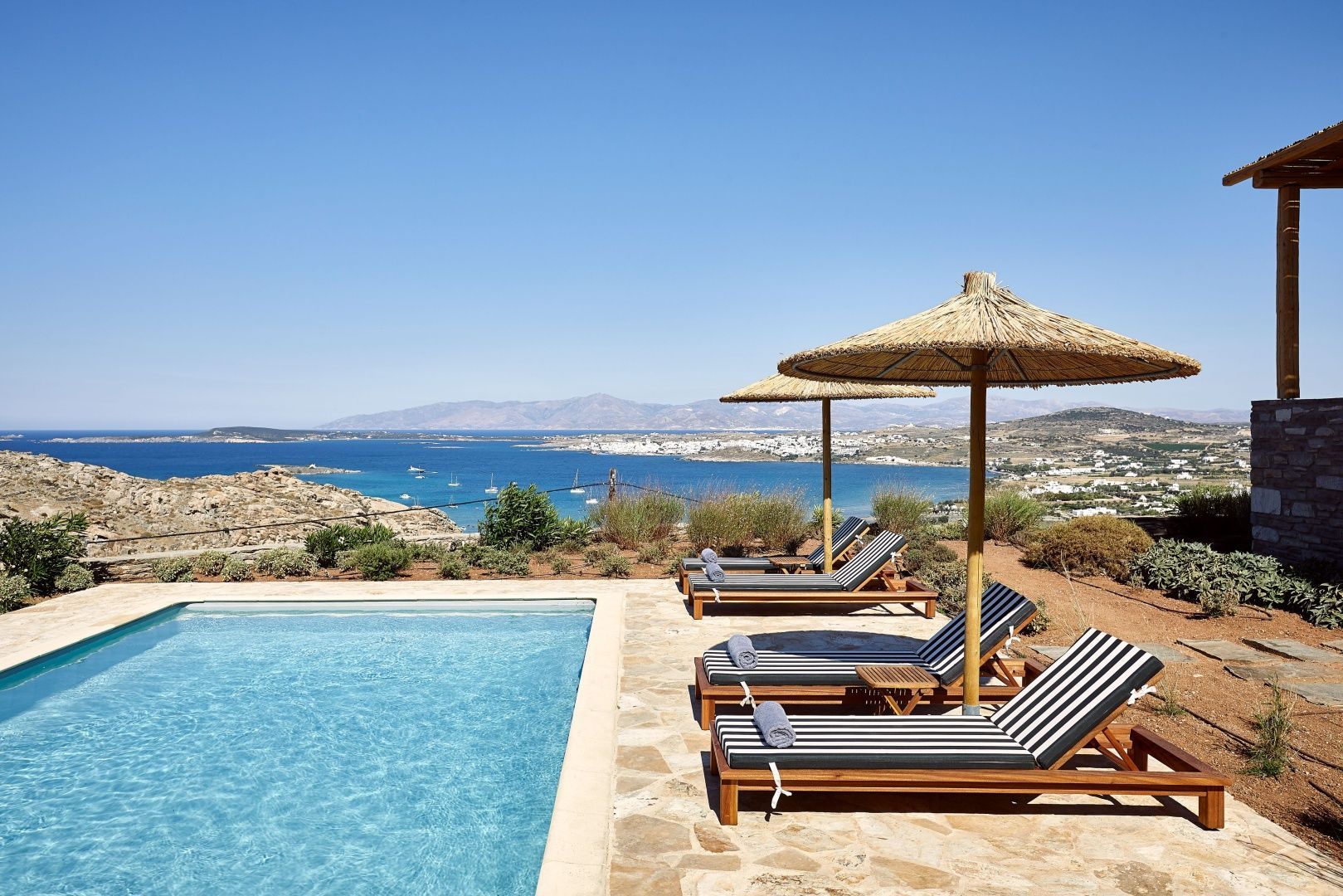 Sonnendeck am Pool mit Liegestühlen, Strohschirmen und Blick auf das Meer.