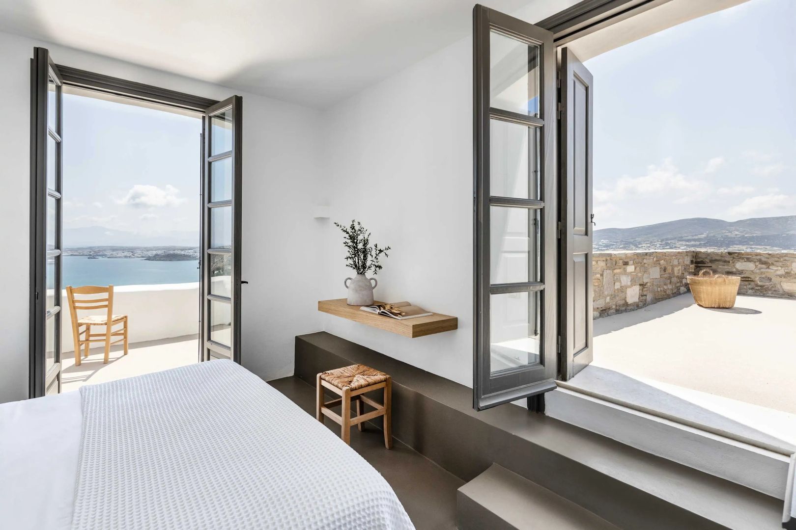 Schlafzimmer mit geöffneten Fenstertüren, die den Blick auf das Meer freigeben.