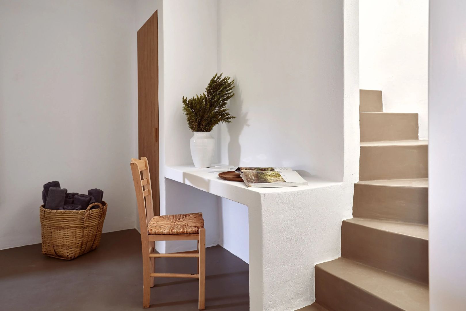 Schreibtischbereich in weißem Zimmer mit Holzstuhl und Treppe ins Obergeschoss.
