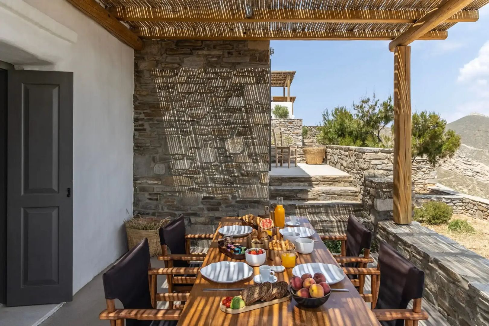 Gedeckter Esstisch aus Holz unter einer Pergola auf der schattigen Terrasse.
