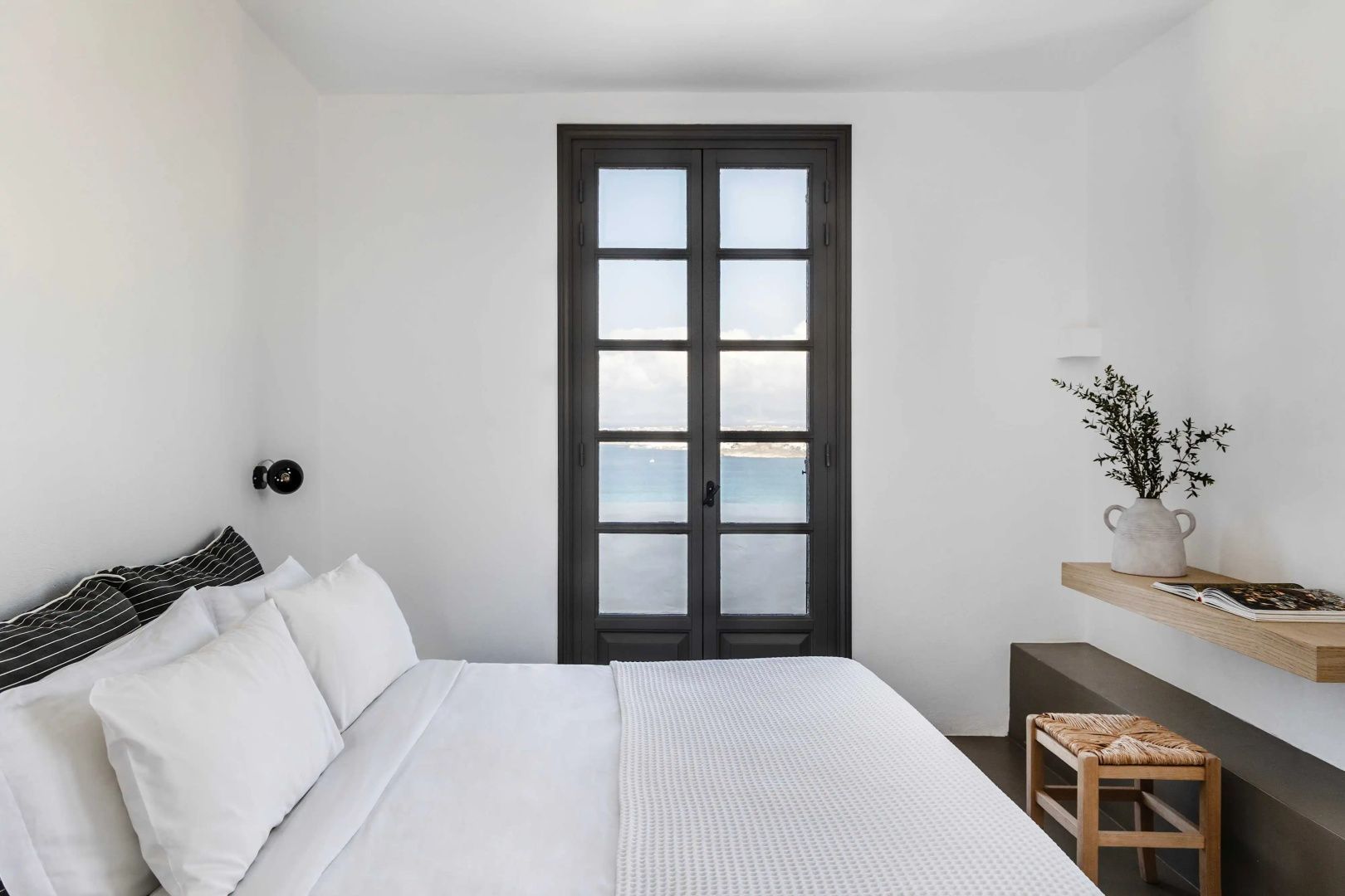 Schlafzimmer mit Doppelbett und Blick durch die geschlossene Glastür auf das Meer.