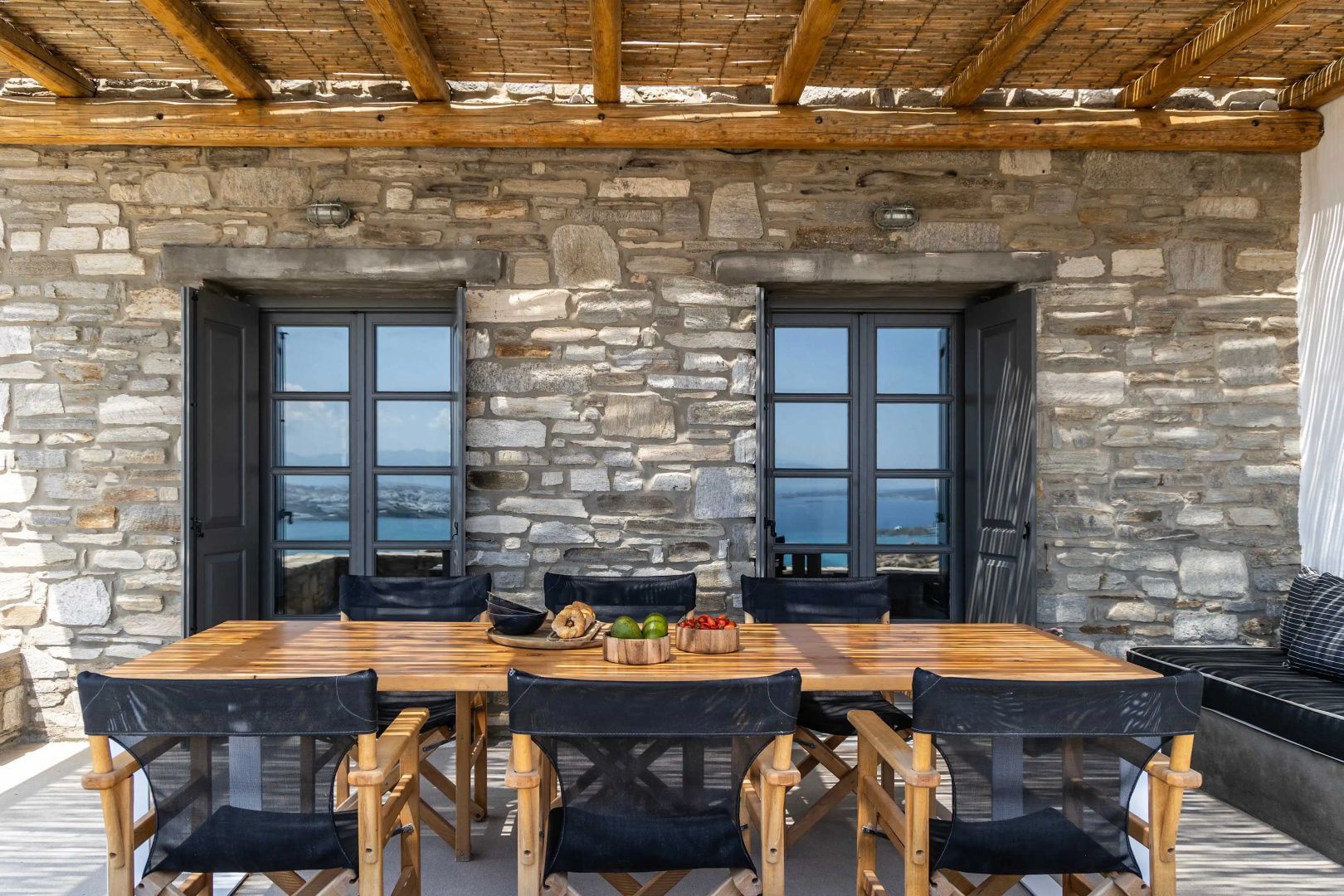 Holztisch mit Stühlen auf einer überdachten Terrasse mit Natursteinwand.