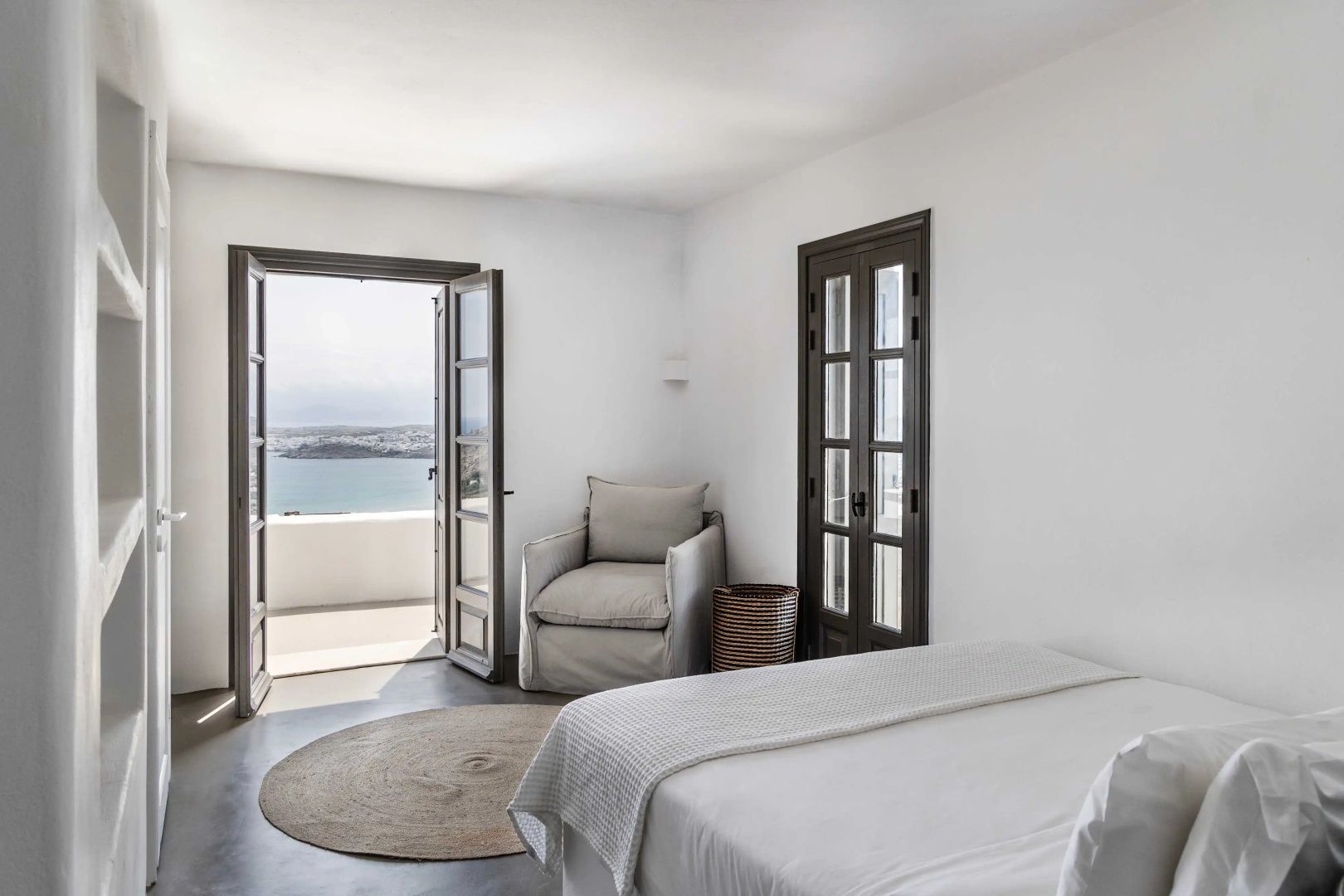 Schlafzimmer mit geöffneter Flügeltür, Sessel und Blick auf das Meer.