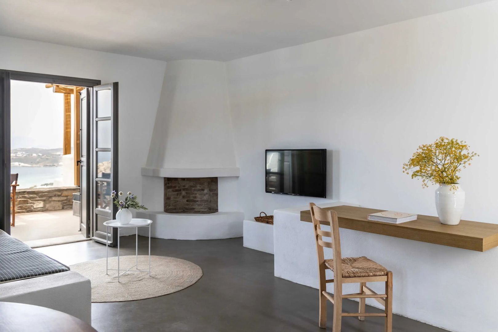 Hell eingerichteter Wohnbereich mit Kamin, Wand-TV und Blick zum Balkon.