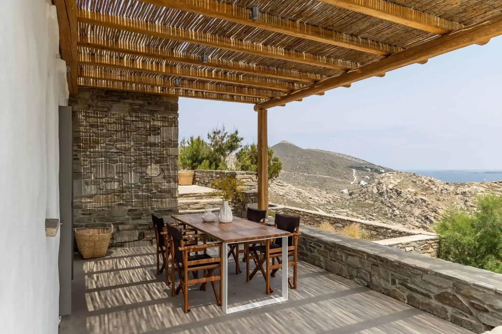 Überdachte Terrasse mit Holz Esstisch und Blick auf die umliegende Hügellandschaft.