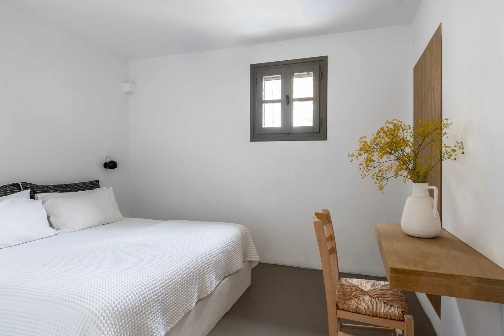 Schlafzimmer mit weißem Bett, Holzschreibtisch und kleinem Fenster.