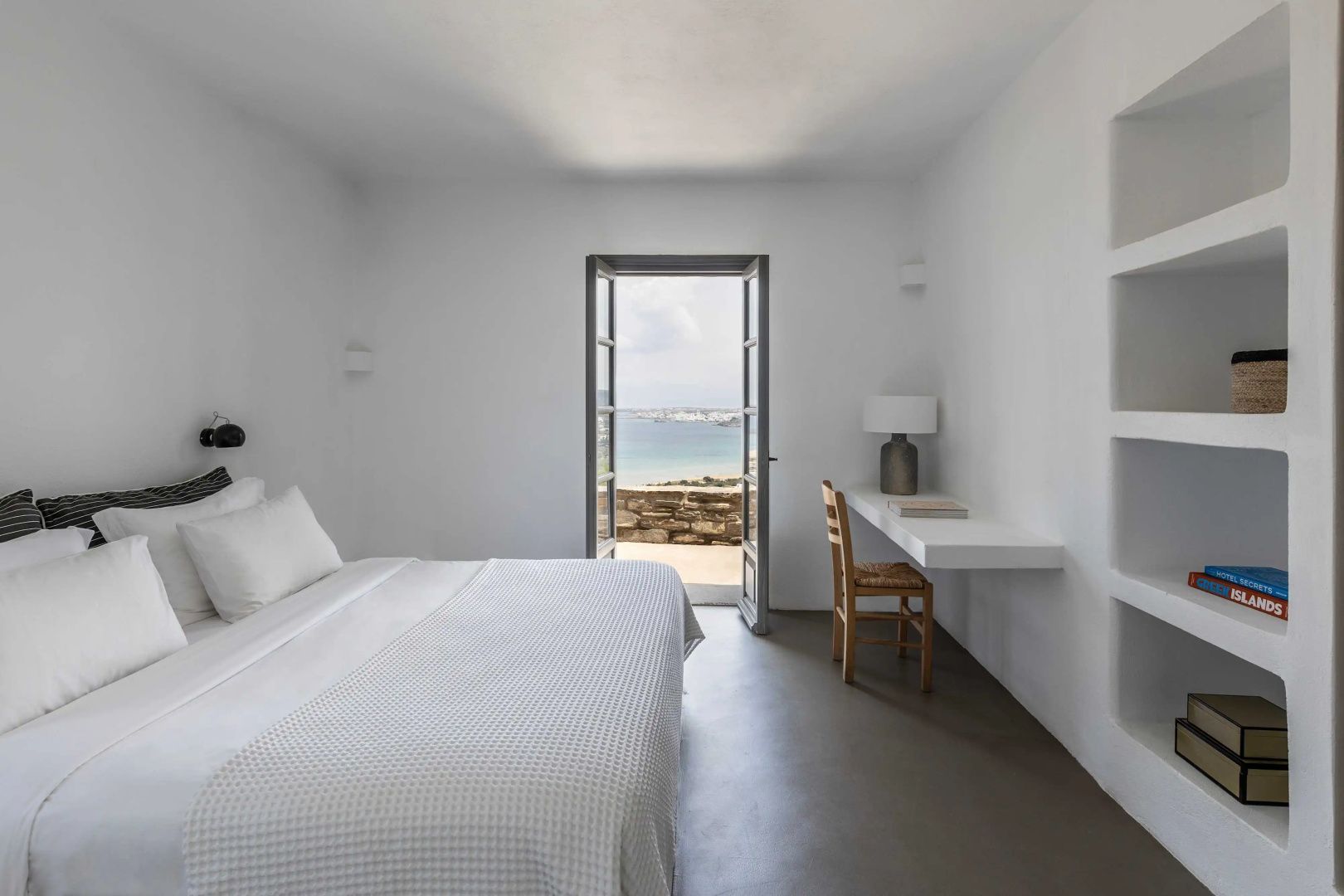 Schlafzimmer mit Schreibtisch und weit geöffneter Balkontür mit Blick auf die Küste.