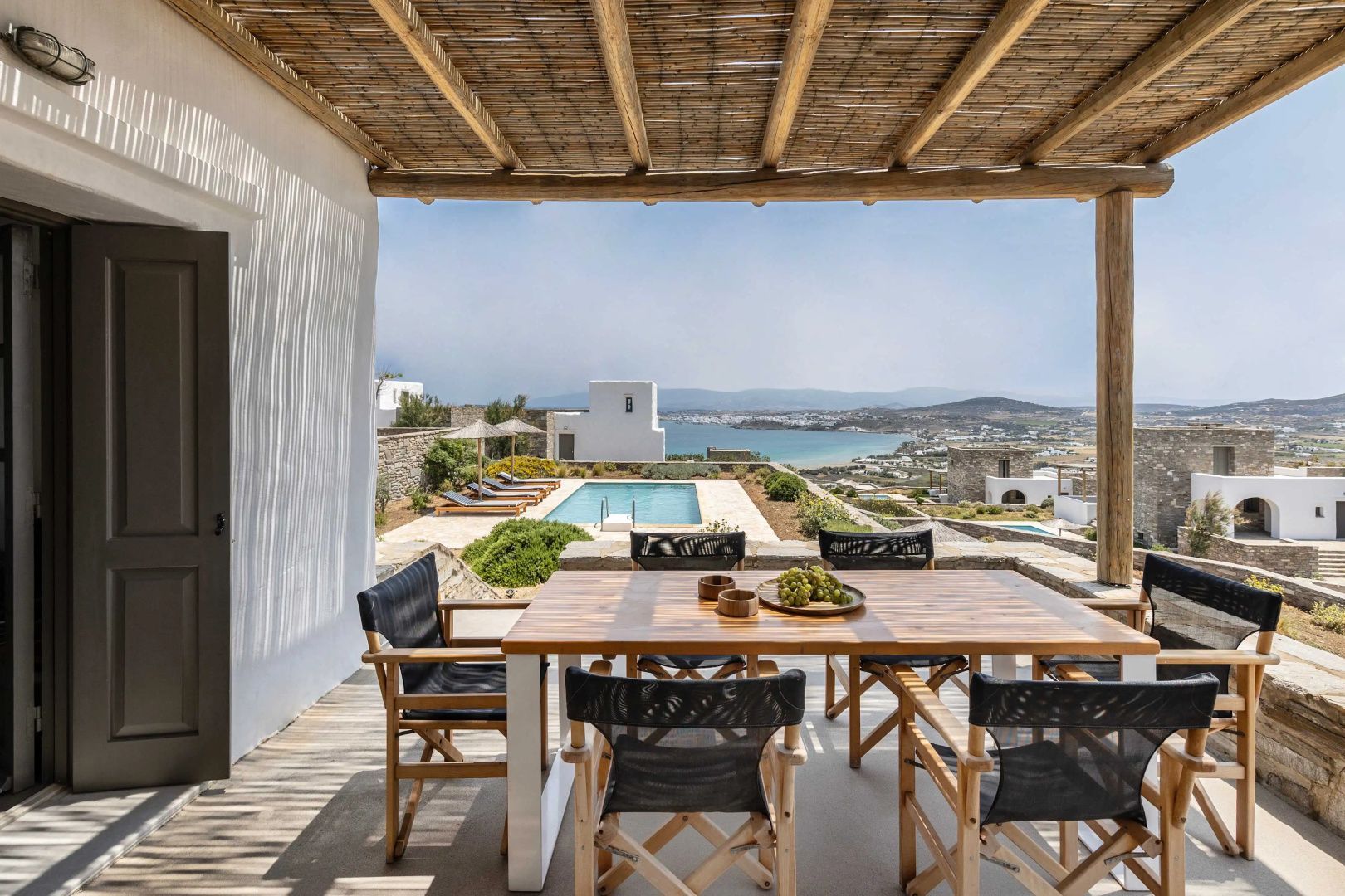Überdachte Terrasse mit Holzmöbeln und Blick auf den Pool sowie das Meer in der Ferne.