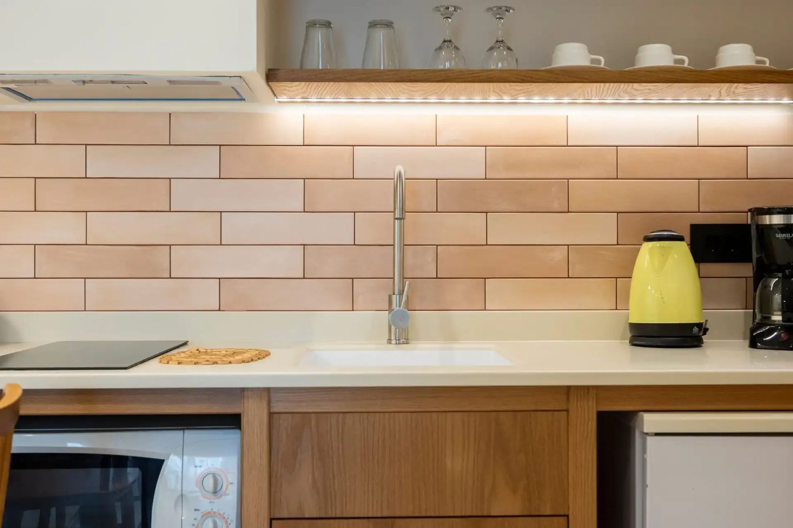 Moderne Küchenzeile mit Spülbecken, hellen Fliesen und Holzregal für Gläser.