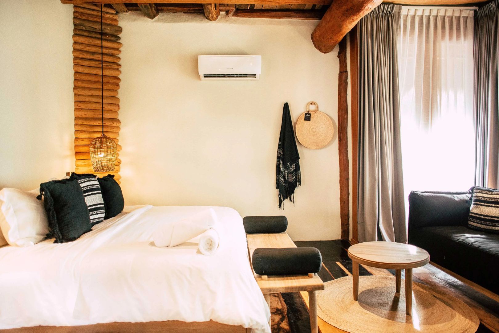 Hotelzimmer mit weiß bezogenem Doppelbett, Holzdecke und dekorativem Flechtwerk an der Wand.