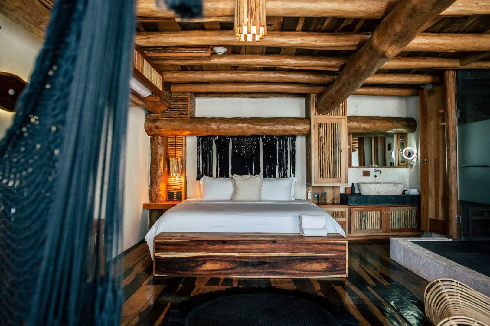 Doppelbett mit weißer Bettwäsche in einem Zimmer mit rustikaler Decke aus dicken Baumstämmen.
