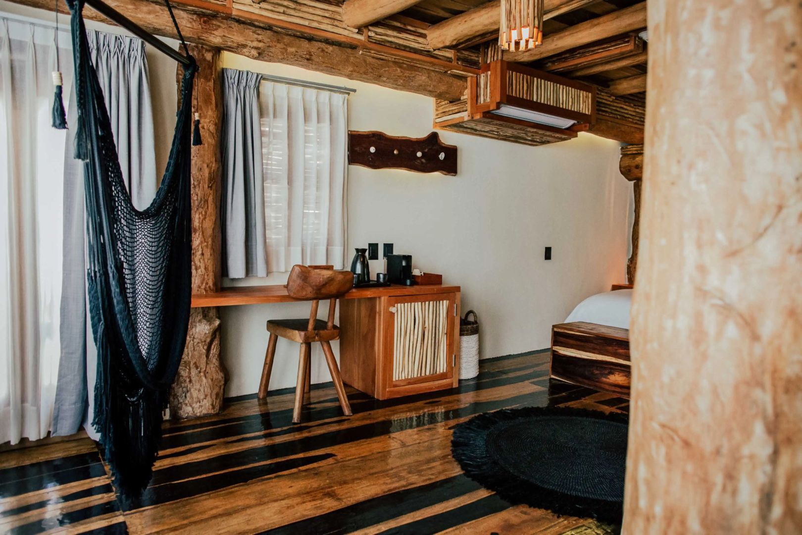 Arbeitsbereich im Zimmer mit Holzschreibtisch, Stuhl, Minibar und schwarzer Hängematte.