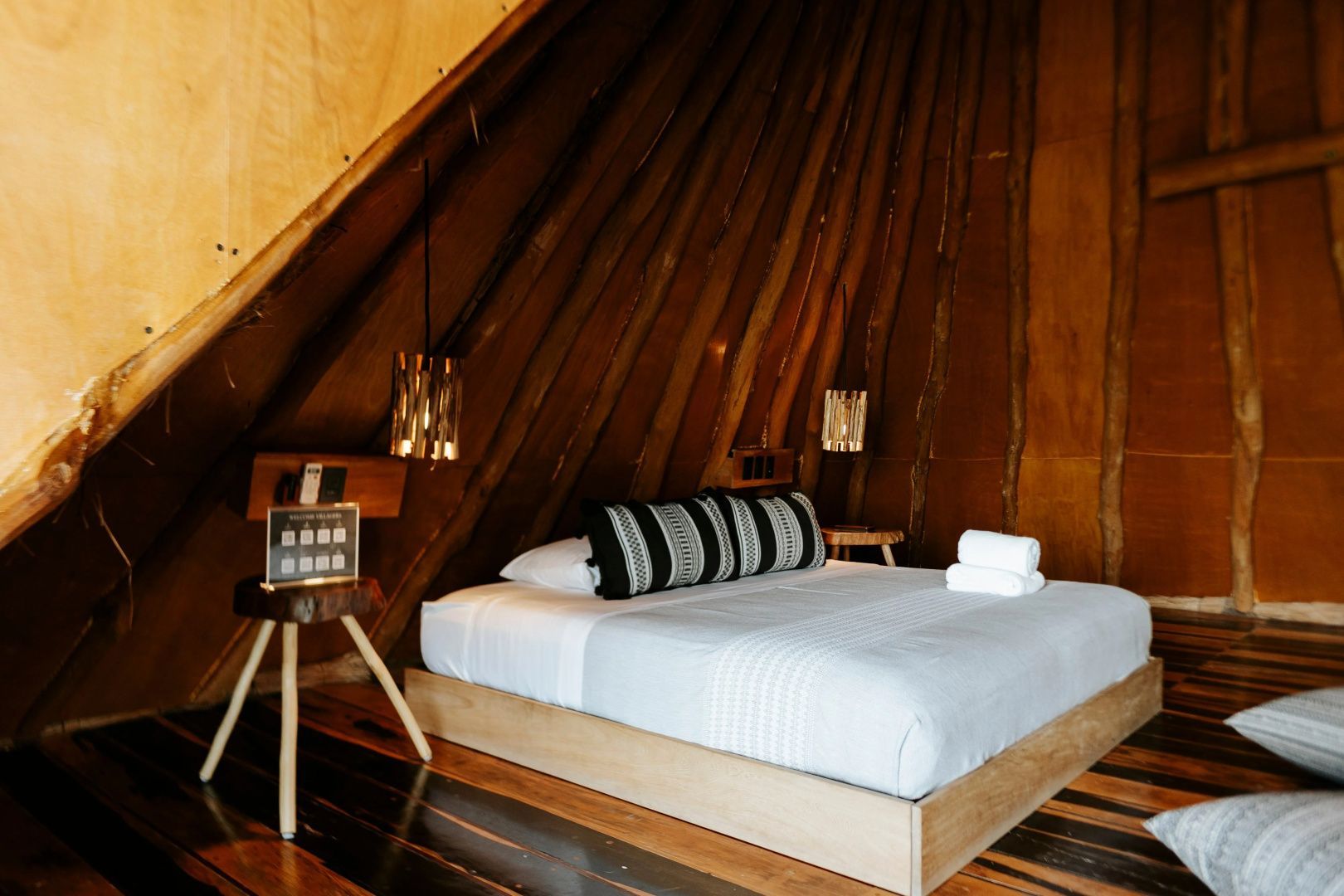 Doppelbett aus Holz in einem rustikalen Zimmer mit spitz zulaufender Holzdecke.