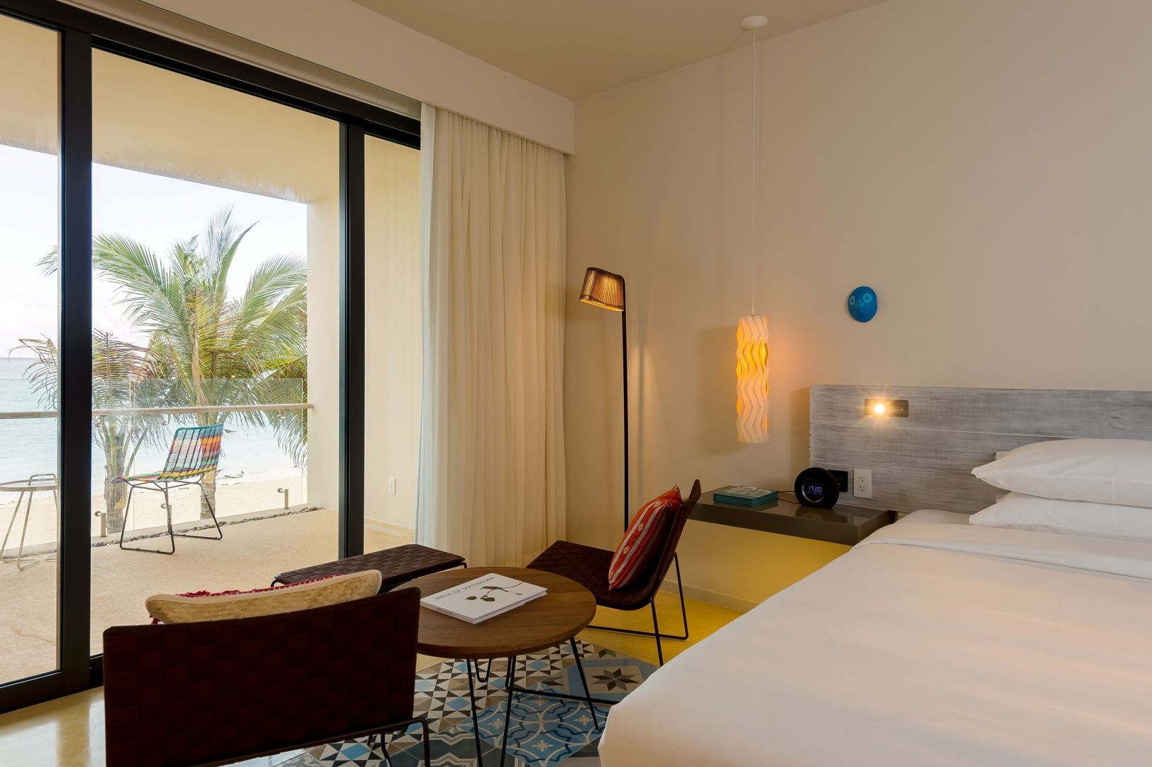 Helles Hotelzimmer mit Doppelbett, Sitzbereich und Balkon mit Blick auf den Strand.
