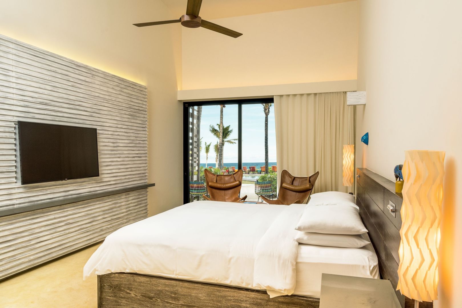 Modernes Hotelzimmer mit Kingsize-Bett, zwei Ledersesseln und Blick auf Garten und Meer.