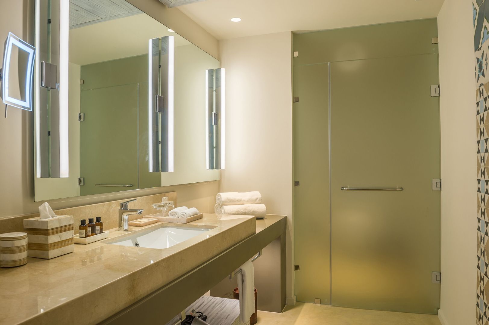 Badezimmer mit Waschtisch aus Naturstein, großem Spiegel und Milchglastür.