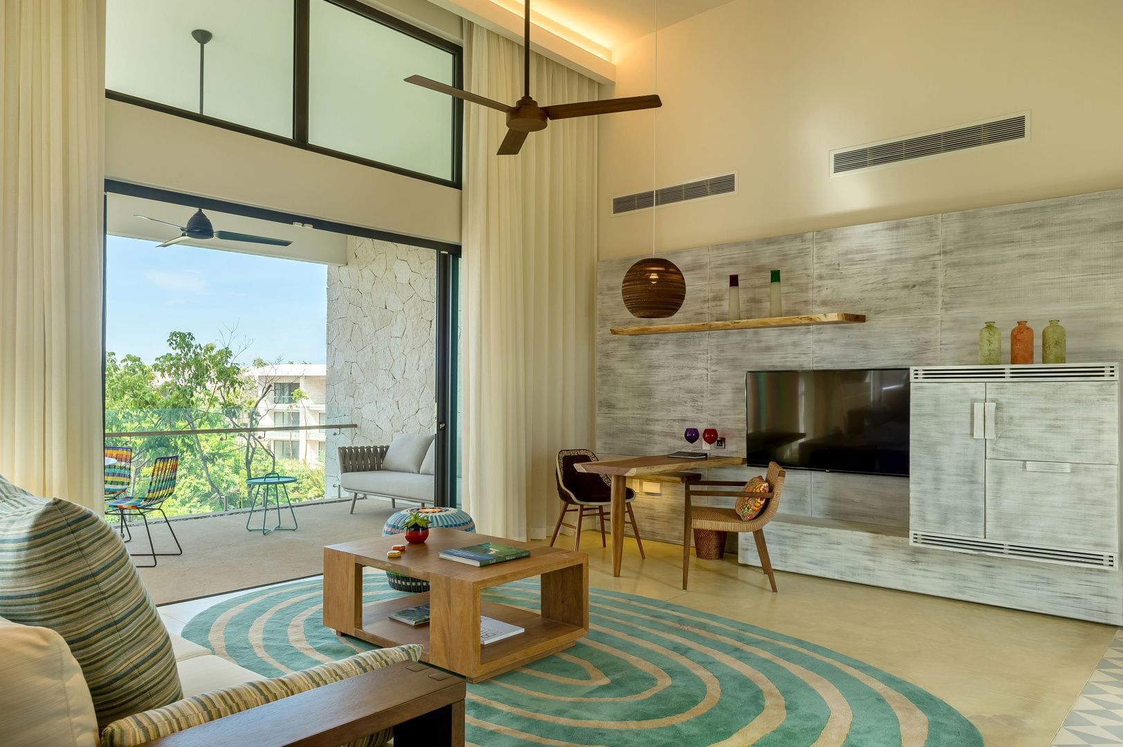 Wohnbereich einer Suite mit Holztisch, flachem Fernseher und Balkon mit Grünblick.