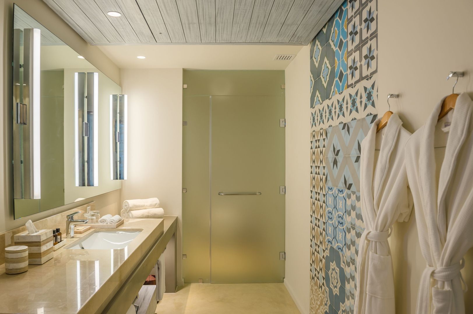 Badezimmer mit gemustertem Fliesendekor, Waschtisch und aufgehängtem Bademantel.