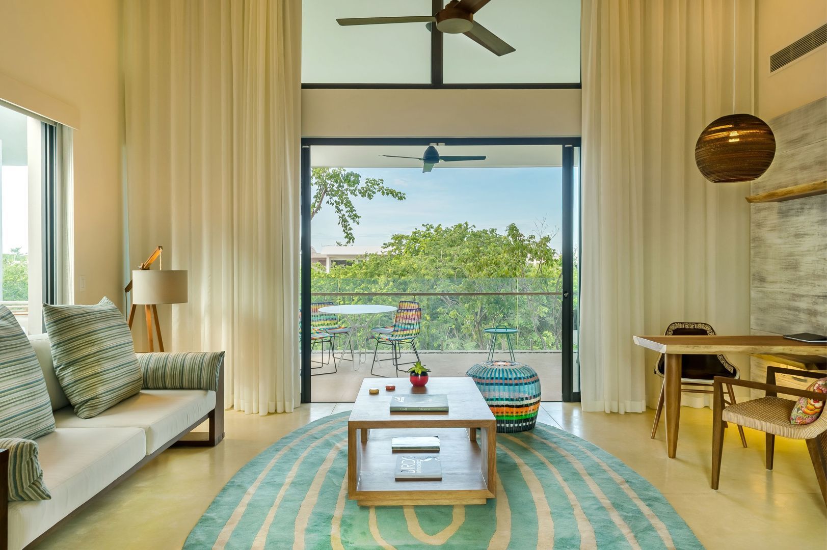 Wohnzimmer mit Holzcouchtisch, buntem Teppich und Blick auf den Balkon im Grünen.