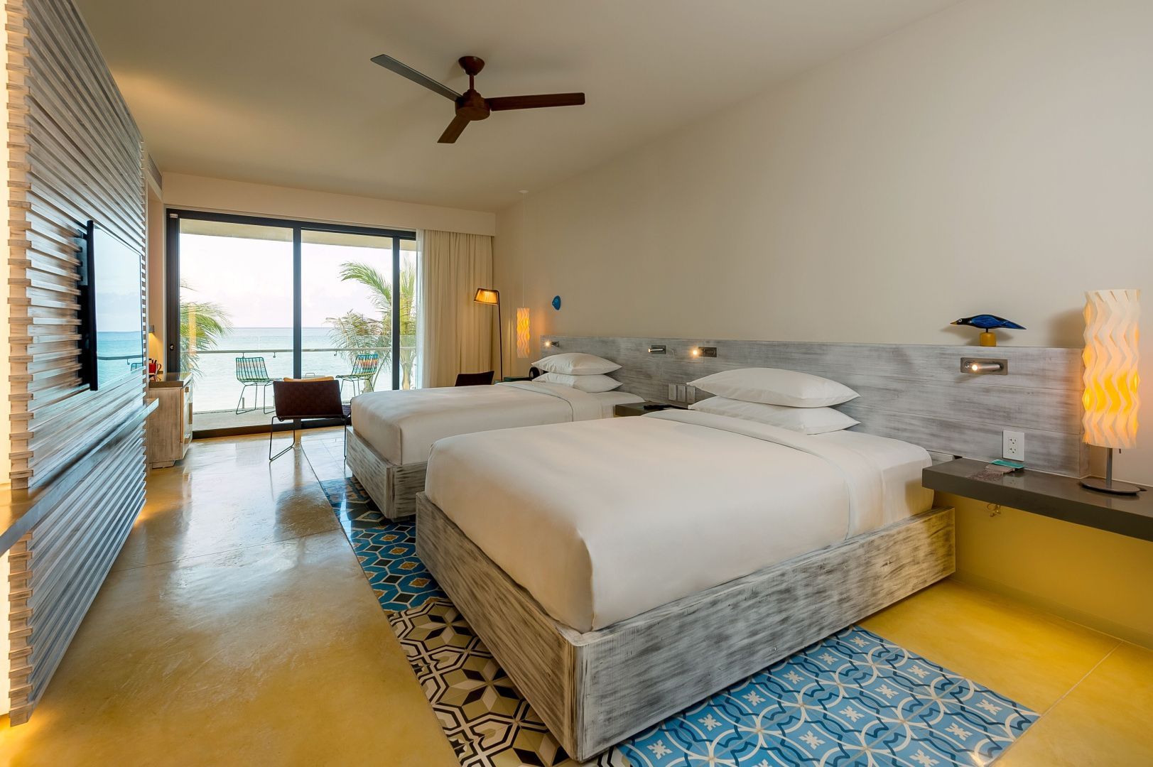 Hotelzimmer mit zwei Doppelbetten, Ventilator und Balkon mit Blick aufs Meer.
