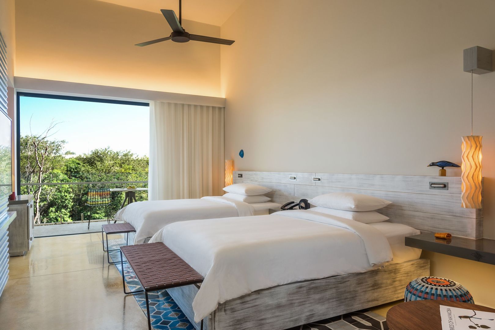 Hell eingerichtetes Hotelzimmer mit zwei Doppelbetten, Deckenventilator und Balkon.