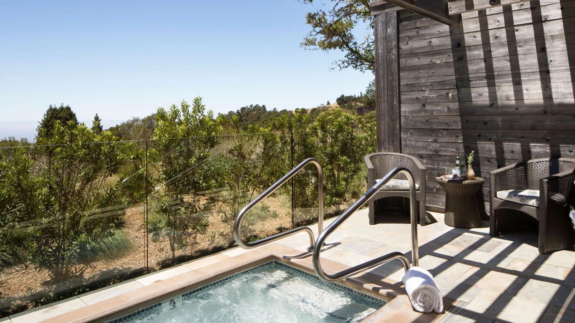 Holzterrasse mit privatem Whirlpool und Blick auf die umliegenden grünen Bäume.