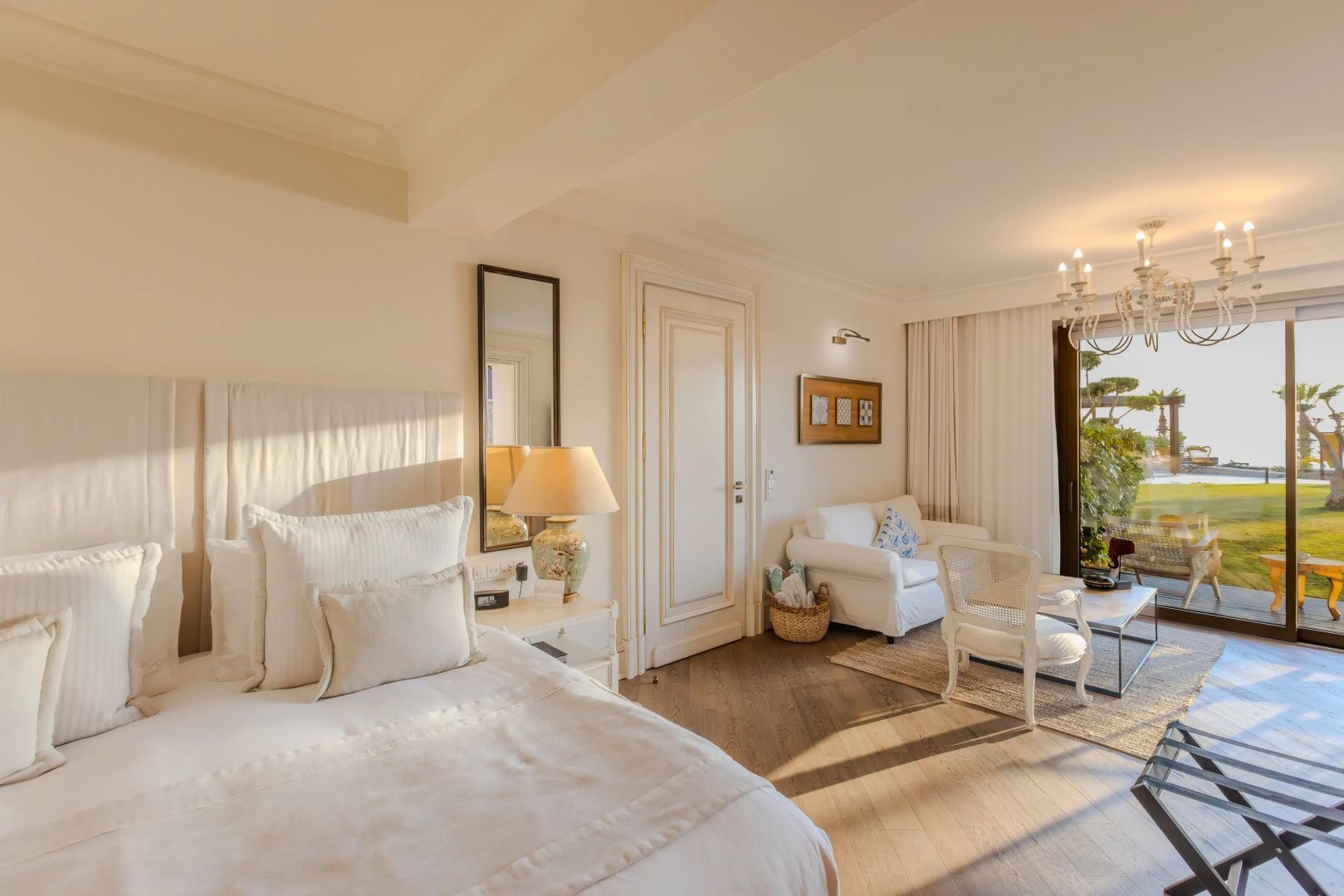 Helles Hotelzimmer mit Parkettboden, Bett, weißem Sofa und großen Fensterfronten.