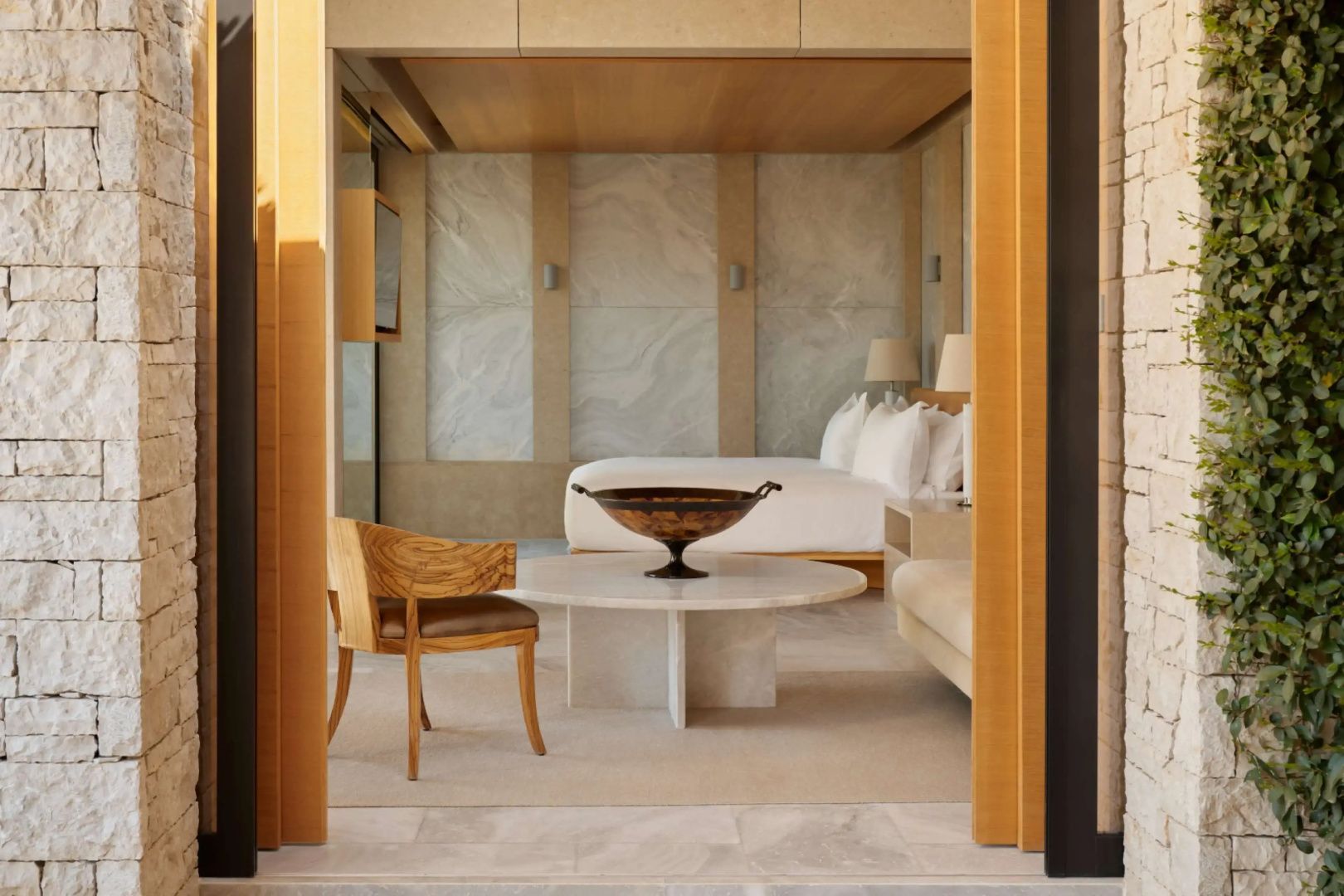 Blick in ein helles Hotelzimmer mit großem Doppelbett, Marmortisch und Holzstuhl.