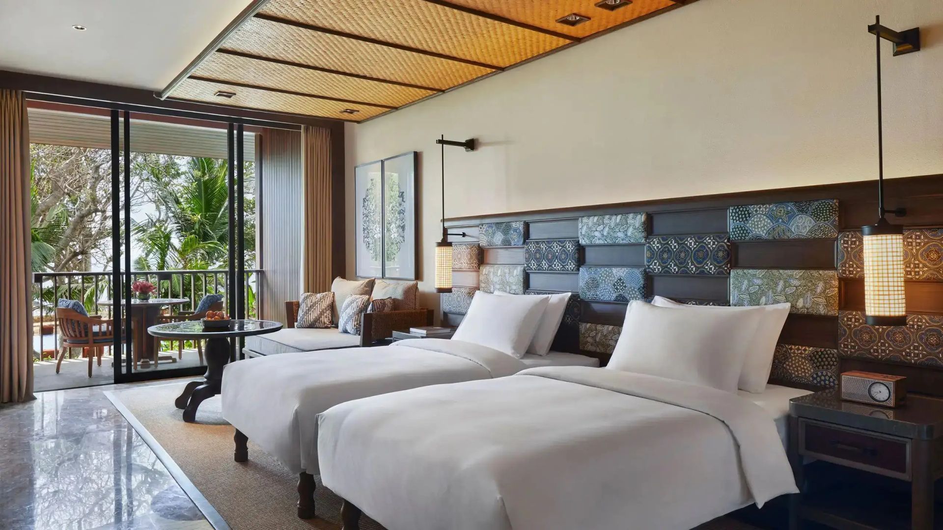 Hotelzimmer mit zwei Einzelbetten, gemustertem Kopfteil und einer Sitzecke neben dem Balkon.