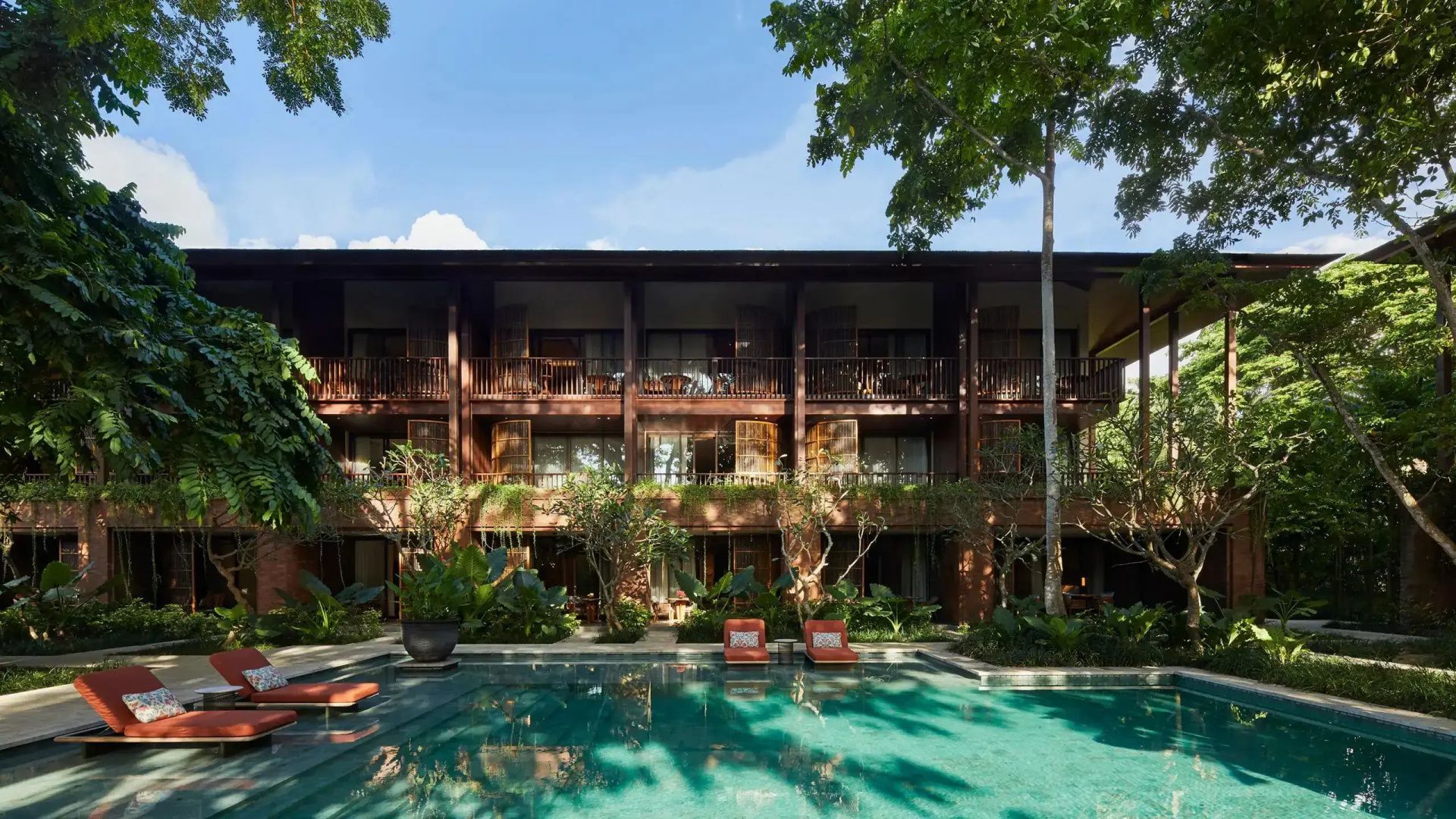 Außenpool des Resorts umgeben von tropischen Pflanzen und zweigeschossigen Holzgebäuden mit Liegen.