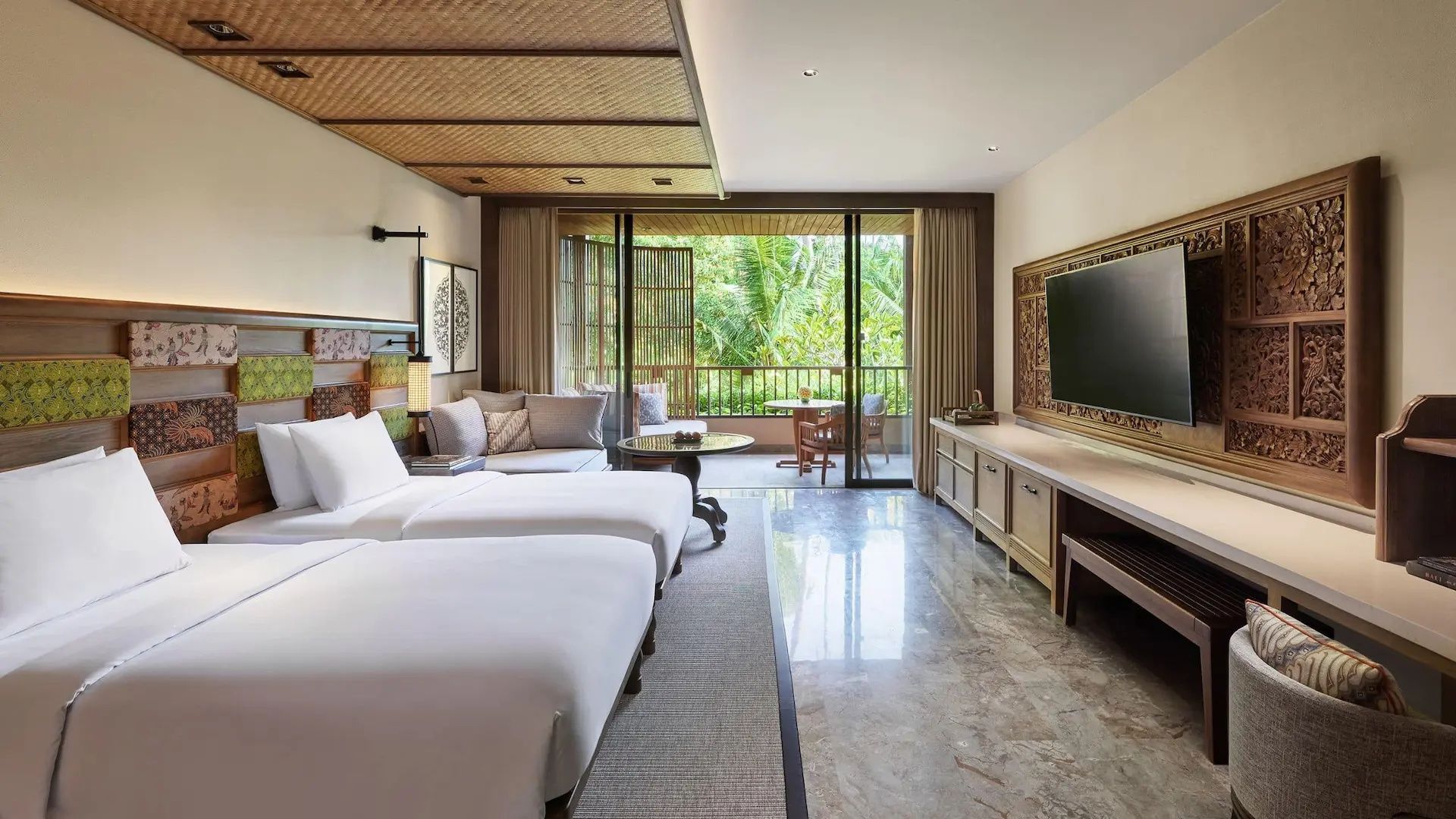Helles Hotelzimmer mit zwei Betten, Fernseher und Balkon mit Blick in die Natur.