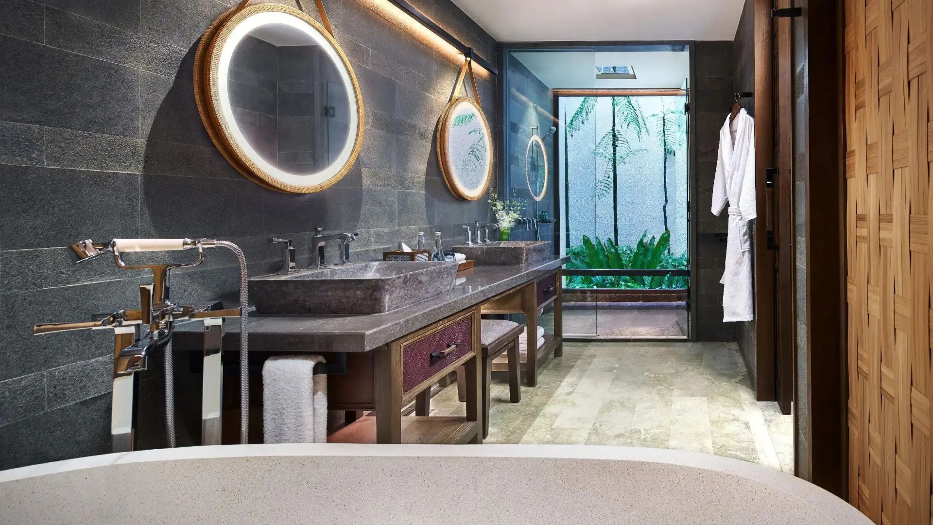 Badezimmer mit zwei Waschtischen, runden Spiegeln und Glasdusche mit Pflanzen.