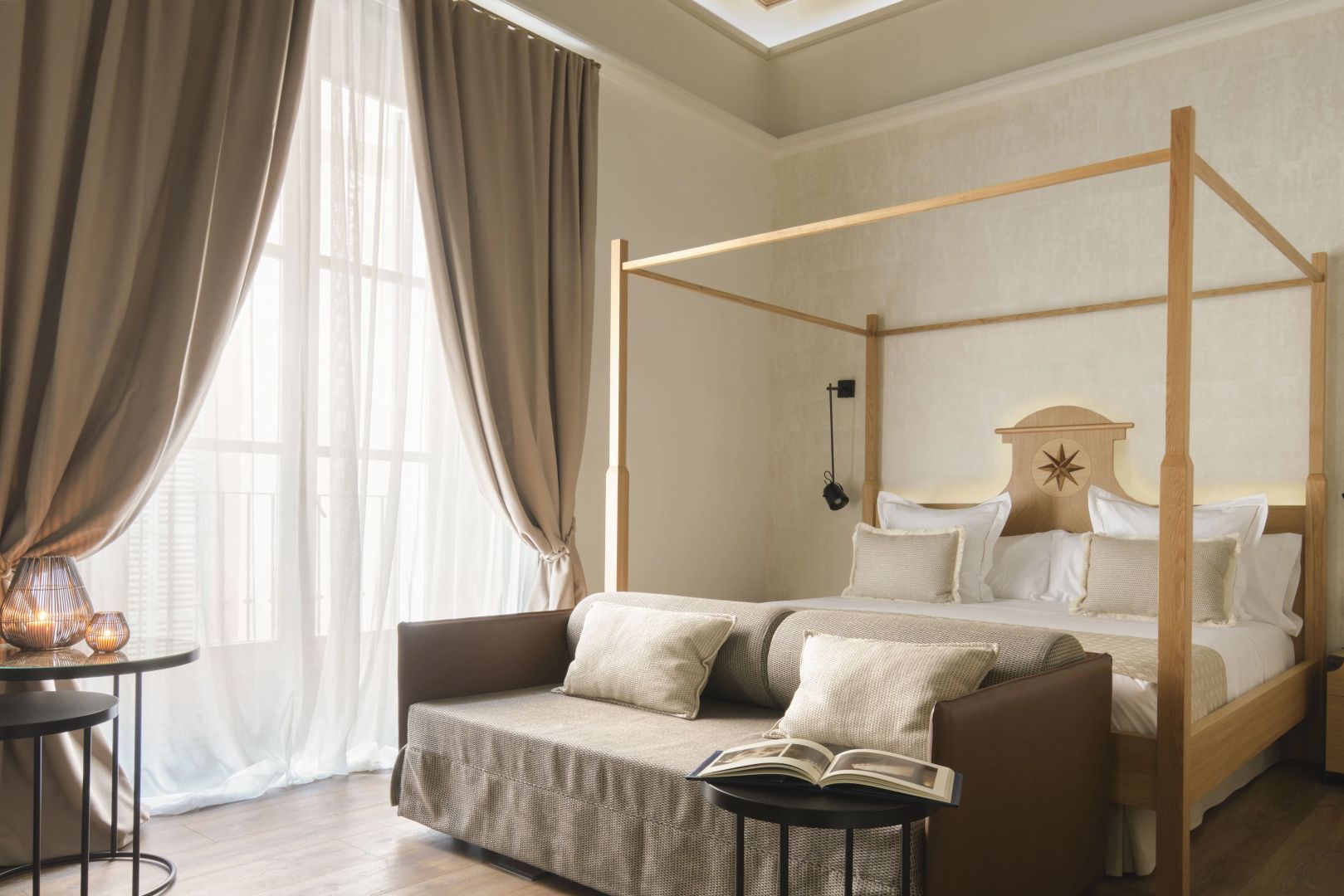 Helles Hotelzimmer mit großem Himmelbett, beigen Vorhängen und einem Sofa im Vordergrund.
