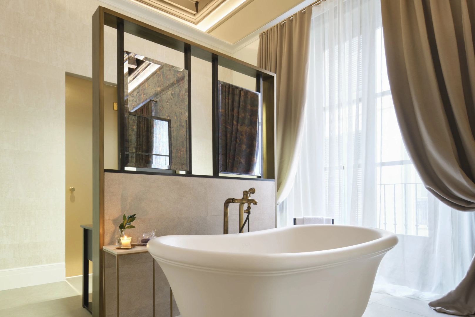 Freistehende weiße Badewanne in einem hellen Badezimmer neben einer Raumtrenner-Wand.