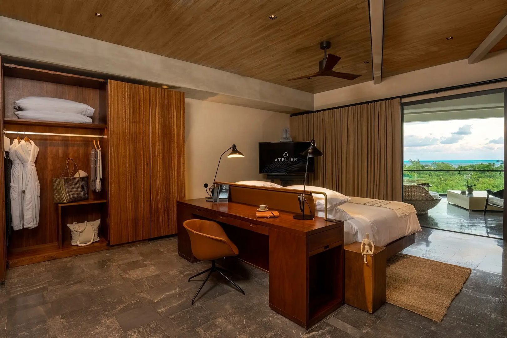 Schlafbereich einer Suite mit Schreibtisch, Stuhl und Doppelbett unter einer Holzbalkendecke.