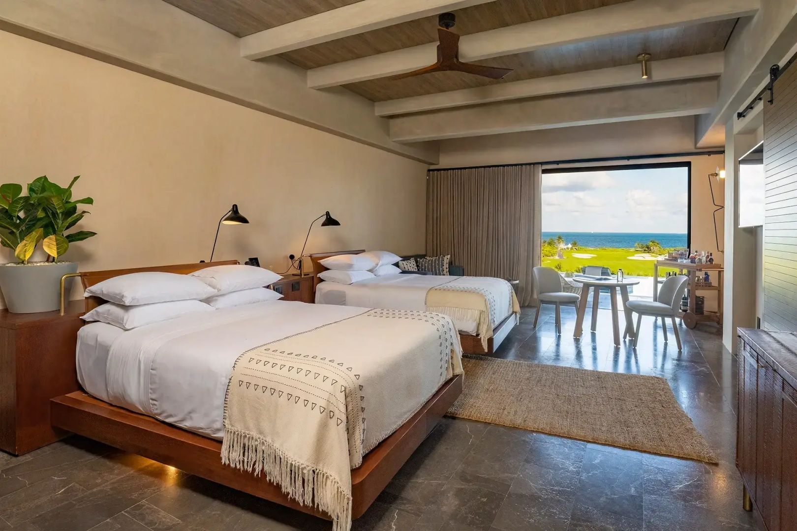Schlafbereich der Suite mit zwei Betten, Holzdecke und Ausblick auf das Meer.