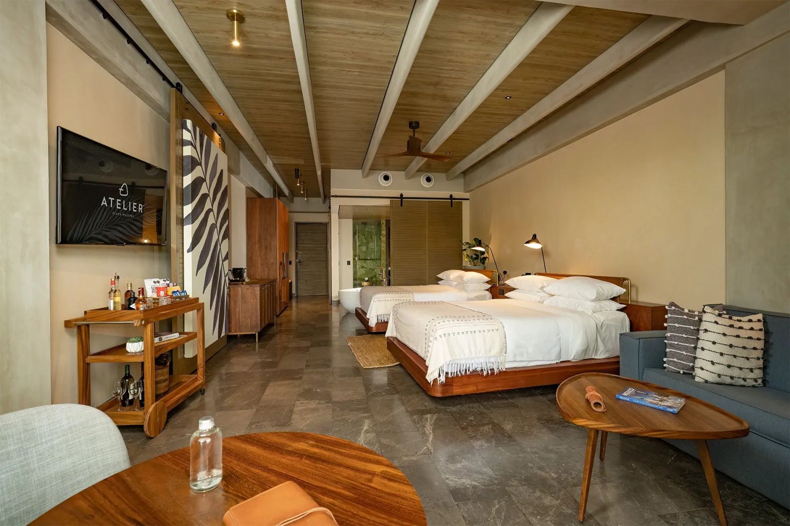 Hotelzimmer mit zwei Doppelbetten, Holzdecke, Ventilator und modernen Sitzmöbeln.